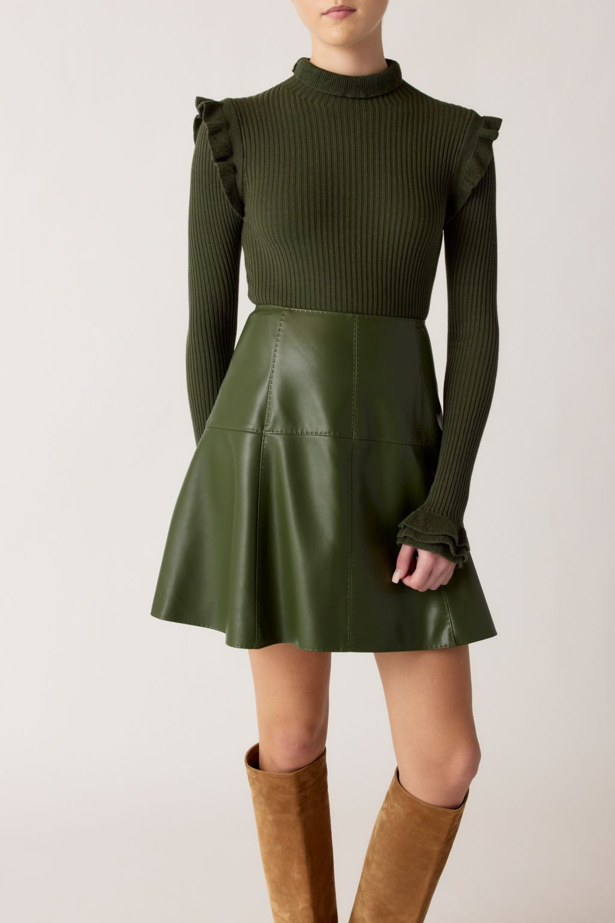 Person wearing a green ribbed sweater and leather skirt with brown knee-high boots on a white background