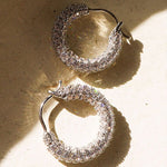 Gold pavé huggie earrings displayed against a warm neutral background