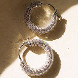 Gold pavé huggie earrings displayed against a warm neutral background