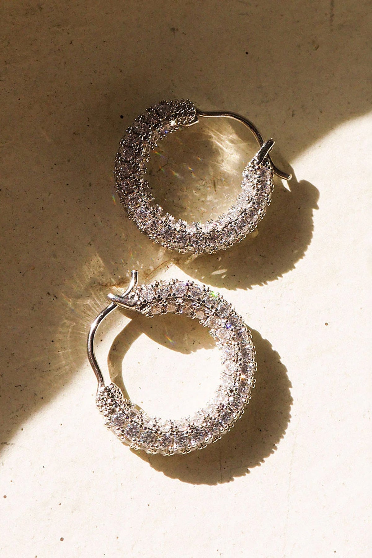 Gold pavé huggie earrings displayed against a warm neutral background