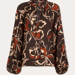 A long-sleeve blouse with a brown base and an abstract floral pattern in beige and rust orange, featuring a tie-neck detail and gathered cuffs, shown against a light gray background.