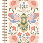 A spiral-bound notebook with a cream-colored cover featuring a symmetrical folk-art design of a decorated bee surrounded by pink flowers and green leaves.