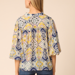 Woman wearing a patterned blouse with blue pants on a beige background