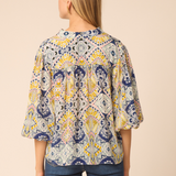 Woman wearing a patterned blouse with blue pants on a beige background