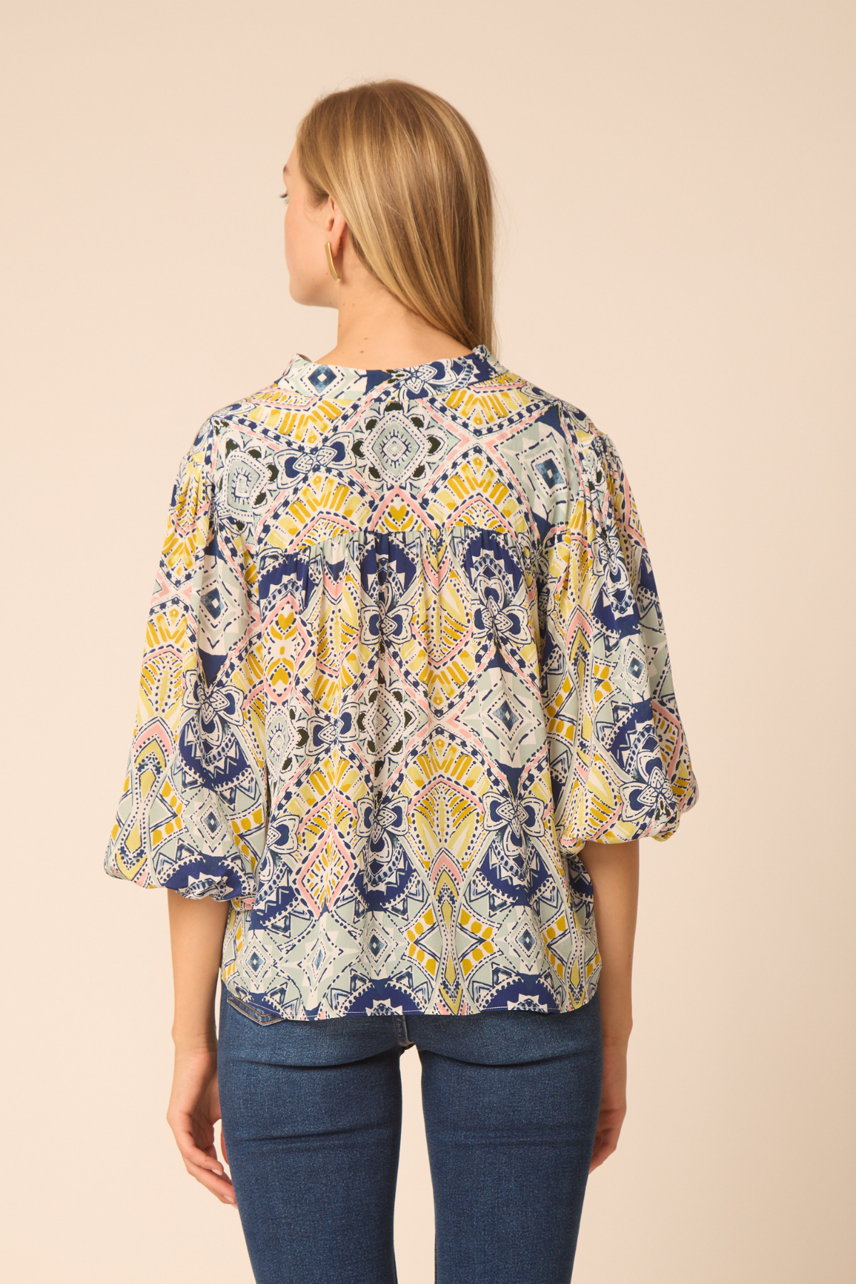 Woman wearing a patterned blouse with blue pants on a beige background