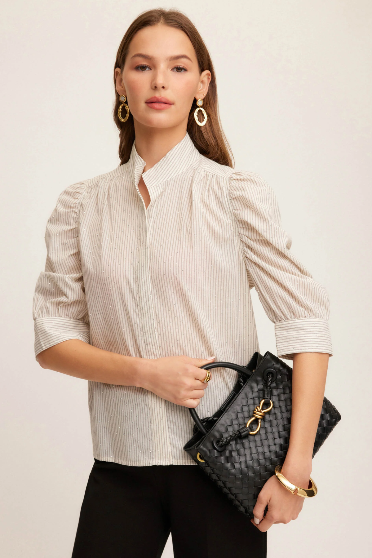Woman holding a black handbag against a plain background