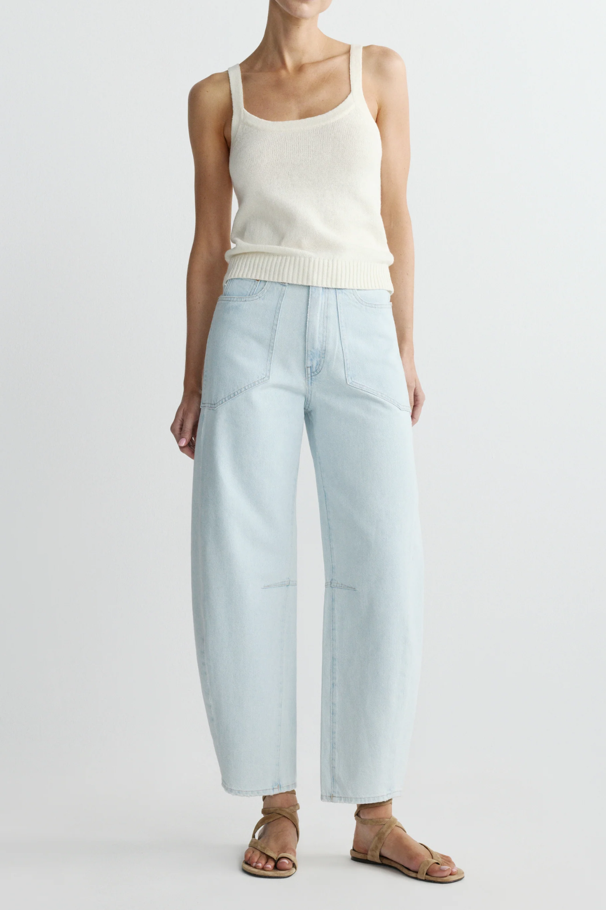 Person wearing a white tank top and light blue pants on a plain background