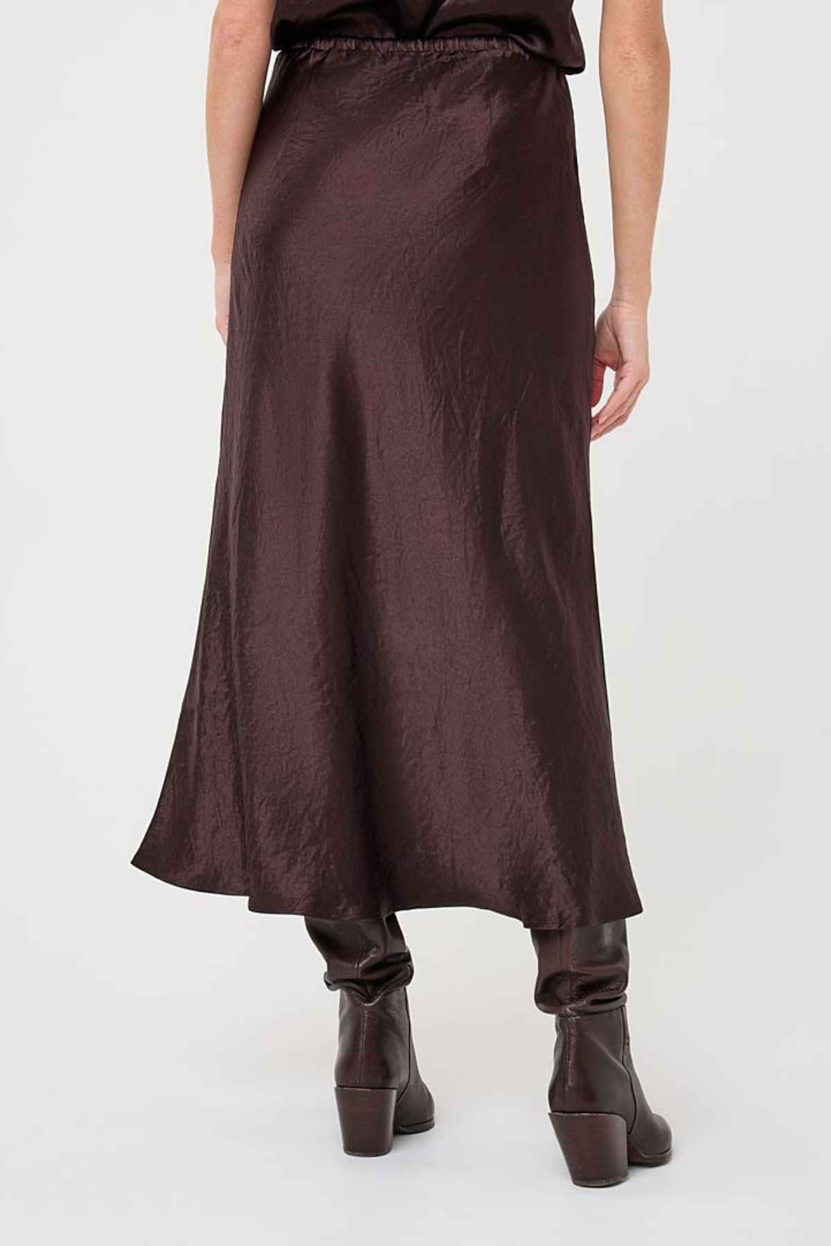 A dark brown satin midi skirt with a crinkled texture, shown on a model from the back against a light gray studio background.
