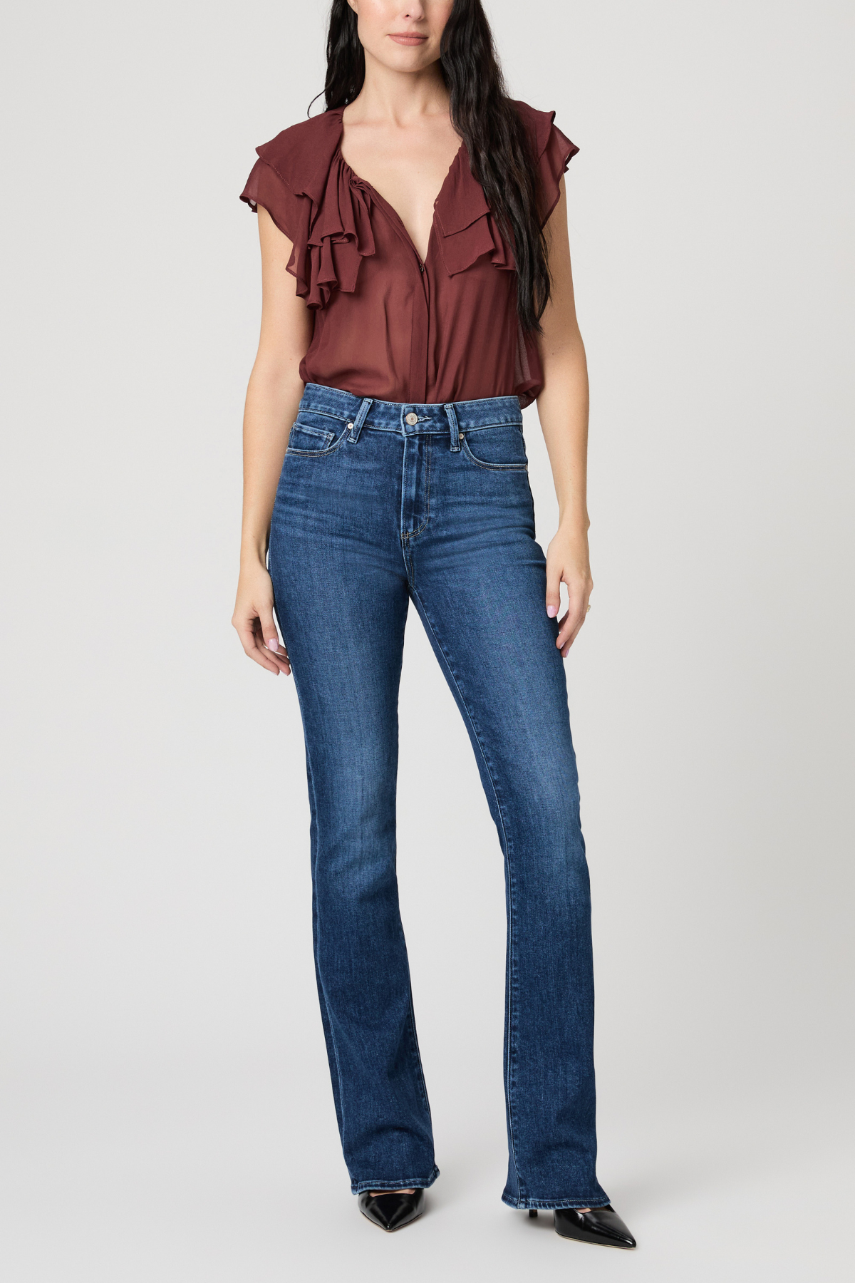 Woman wearing a burgundy ruffled top and blue jeans on a white background