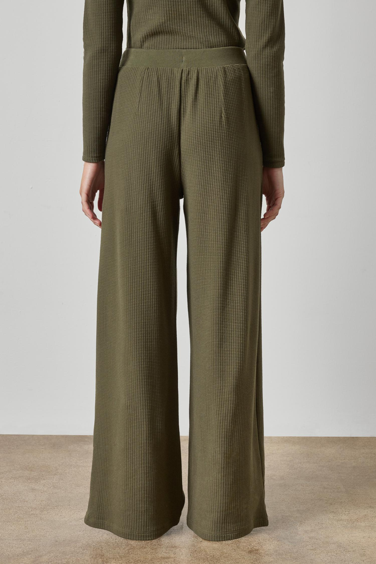 Person wearing olive green ribbed pants and top on a plain background