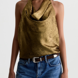 A woman wearing a metallic gold halter top with a textured, crinkled finish, paired with blue jeans and a brown belt, against a plain light gray background.