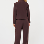 A woman shown from the back wearing a matching dark plum-brown two-piece suit, consisting of a cropped long-sleeve jacket and wide-leg trousers, against a plain white studio background.