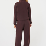 A woman shown from the back wearing a matching dark plum-brown two-piece suit, consisting of a cropped long-sleeve jacket and wide-leg trousers, against a plain white studio background.
