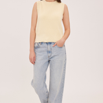 A woman modeling a pale yellow sleeveless knit top with light-wash wide-leg jeans and brown shoes, standing against a plain light background.