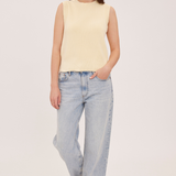 A woman modeling a pale yellow sleeveless knit top with light-wash wide-leg jeans and brown shoes, standing against a plain light background.