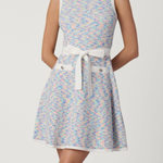 Woman wearing a patterned dress with a white belt on a plain background