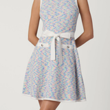 Woman wearing a patterned dress with a white belt on a plain background