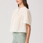 Woman wearing a light-colored blouse and light green pants on a plain background