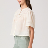Woman wearing a light-colored blouse and light green pants on a plain background