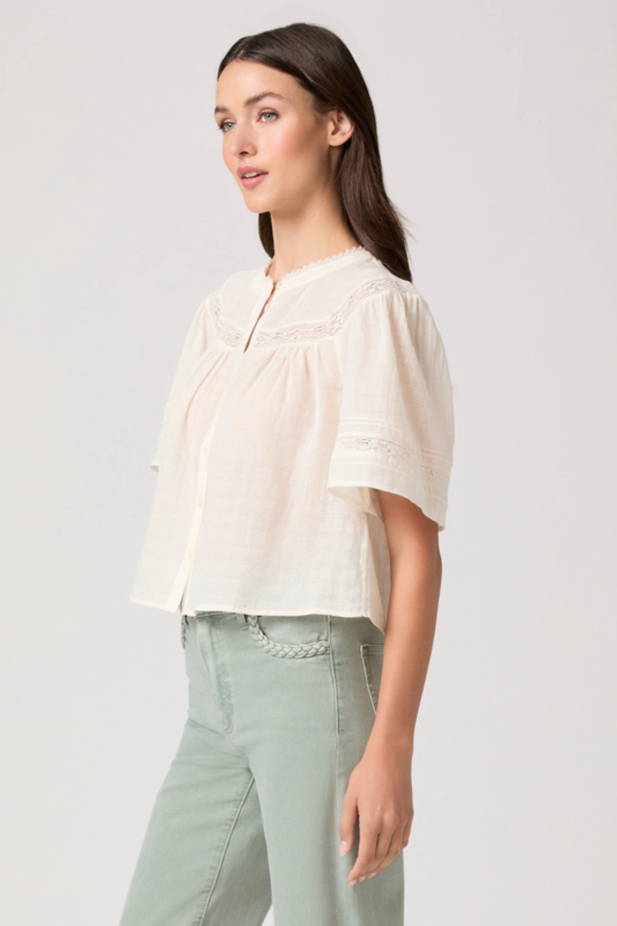 Woman wearing a light-colored blouse and light green pants on a plain background