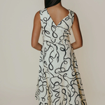 Woman wearing a white dress with black abstract pattern against a plain background