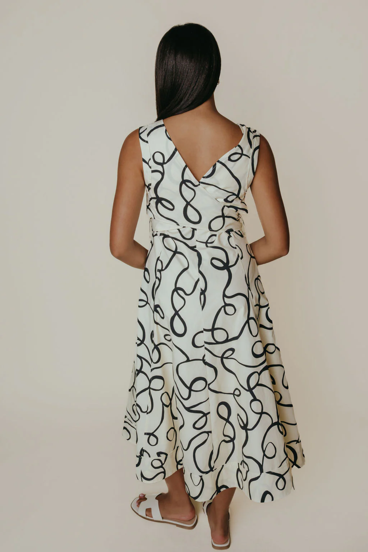 Woman wearing a white dress with black abstract pattern against a plain background