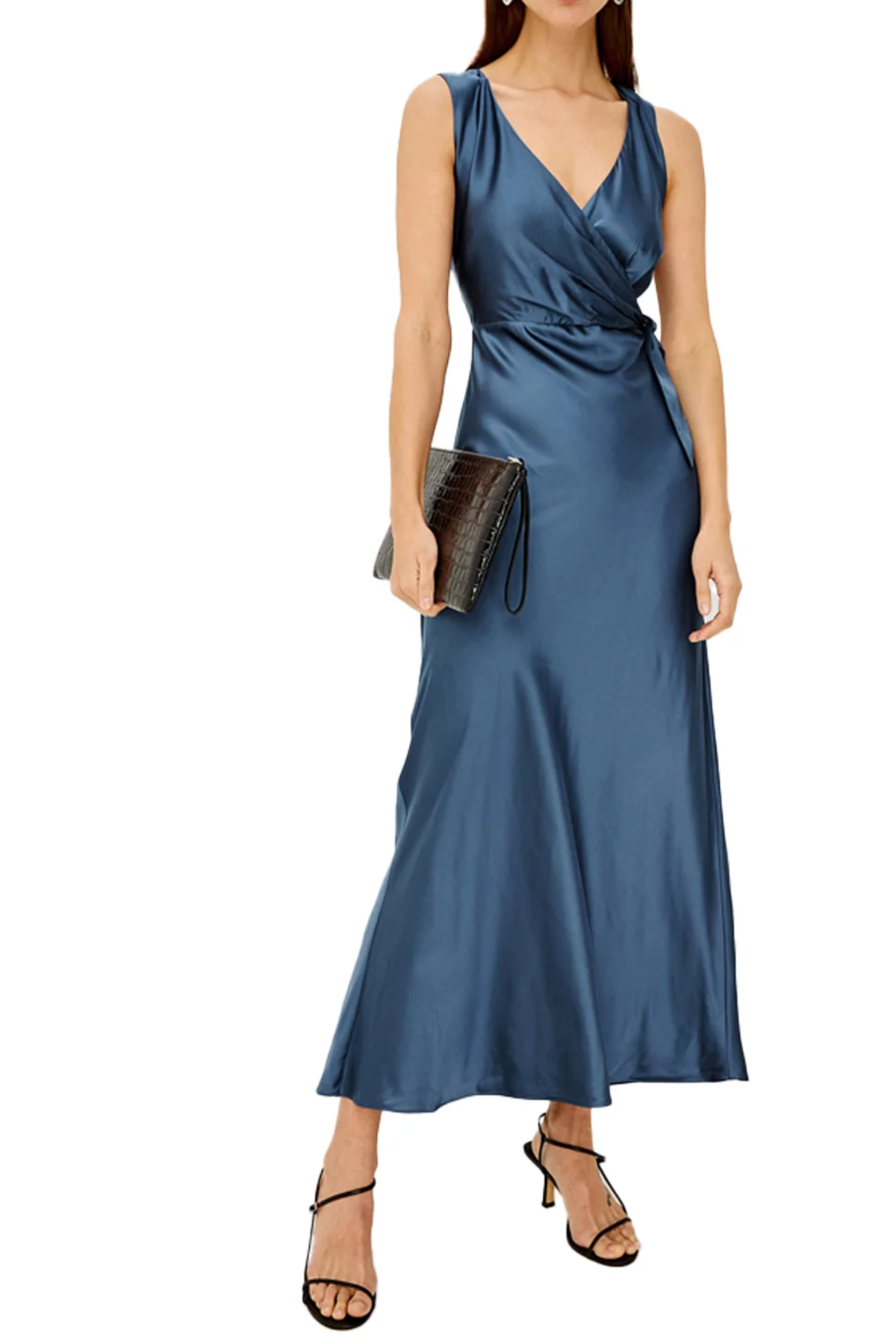 A woman modeling a sleeveless, wrap-style maxi dress in a satin-like blue fabric, holding a dark clutch and wearing black strappy heels against a plain white background.