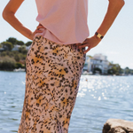 Person wearing a pink top and leopard print skirt by a body of water.