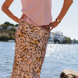 Person wearing a pink top and leopard print skirt by a body of water.