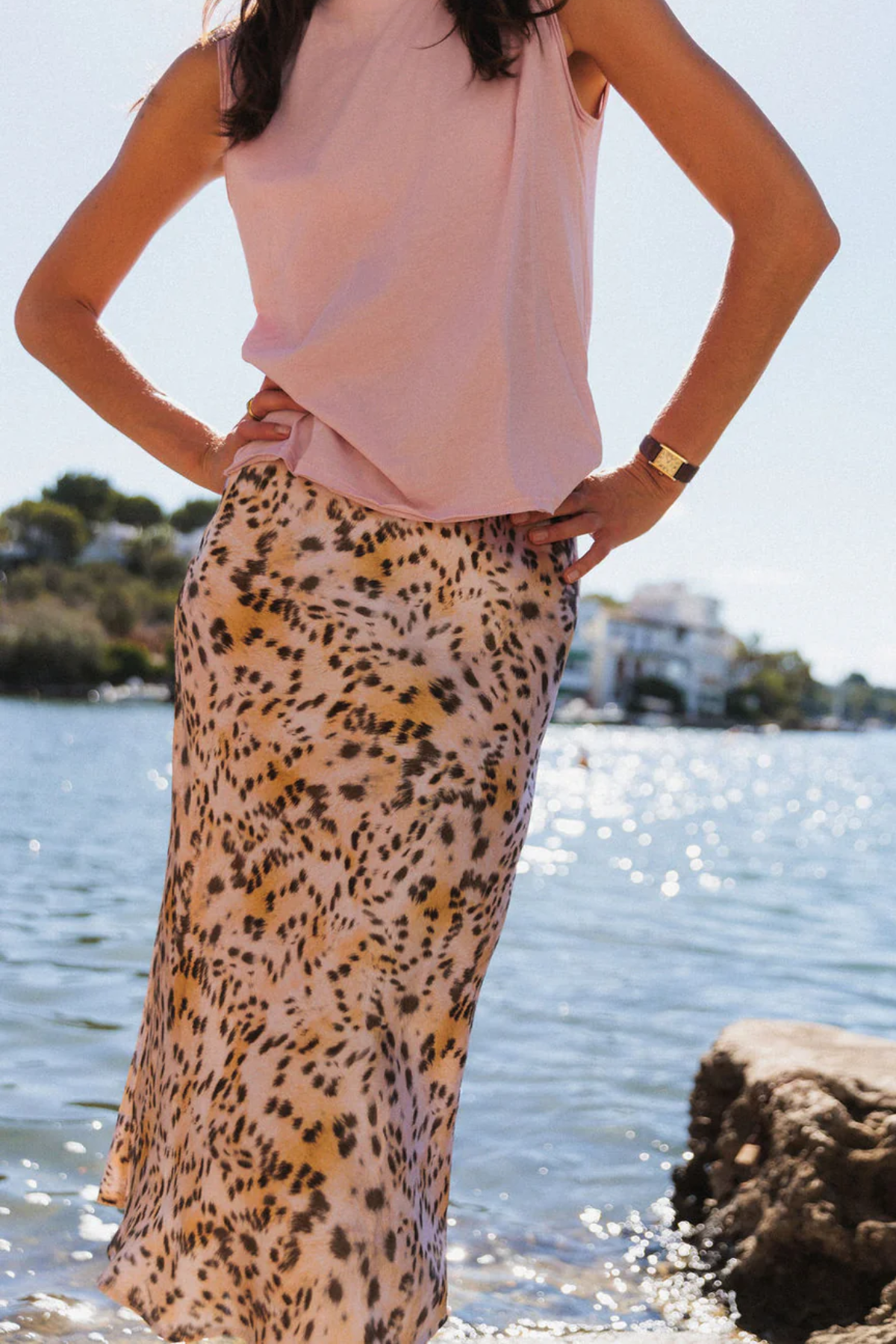 Person wearing a pink top and leopard print skirt by a body of water.