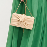 Beige handbag with a chain strap held by a person wearing a green dress.