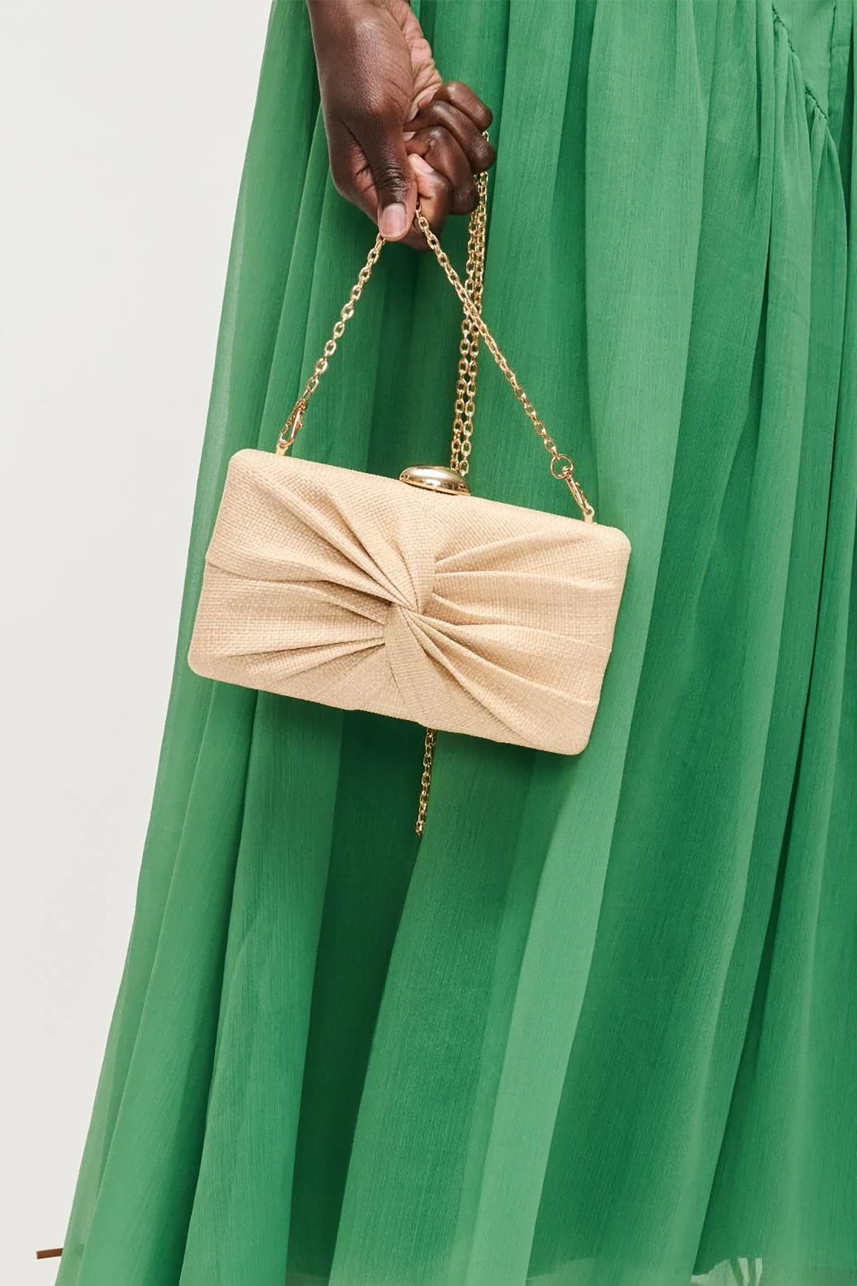 Beige handbag with a chain strap held by a person wearing a green dress.