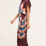 A woman modeling a short-sleeve midi dress with a dark burgundy base and a large abstract floral print in peach, pink, and blue. She is wearing beige heeled mule sandals against a plain light background.