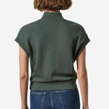 A woman viewed from the back wearing a dark olive green short-sleeve mock-neck knit top and blue jeans against a plain light background.