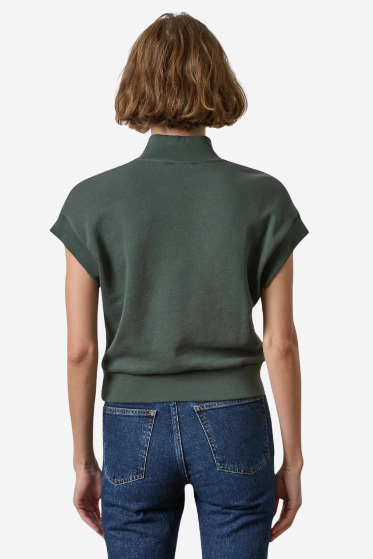 A woman viewed from the back wearing a dark olive green short-sleeve mock-neck knit top and blue jeans against a plain light background.