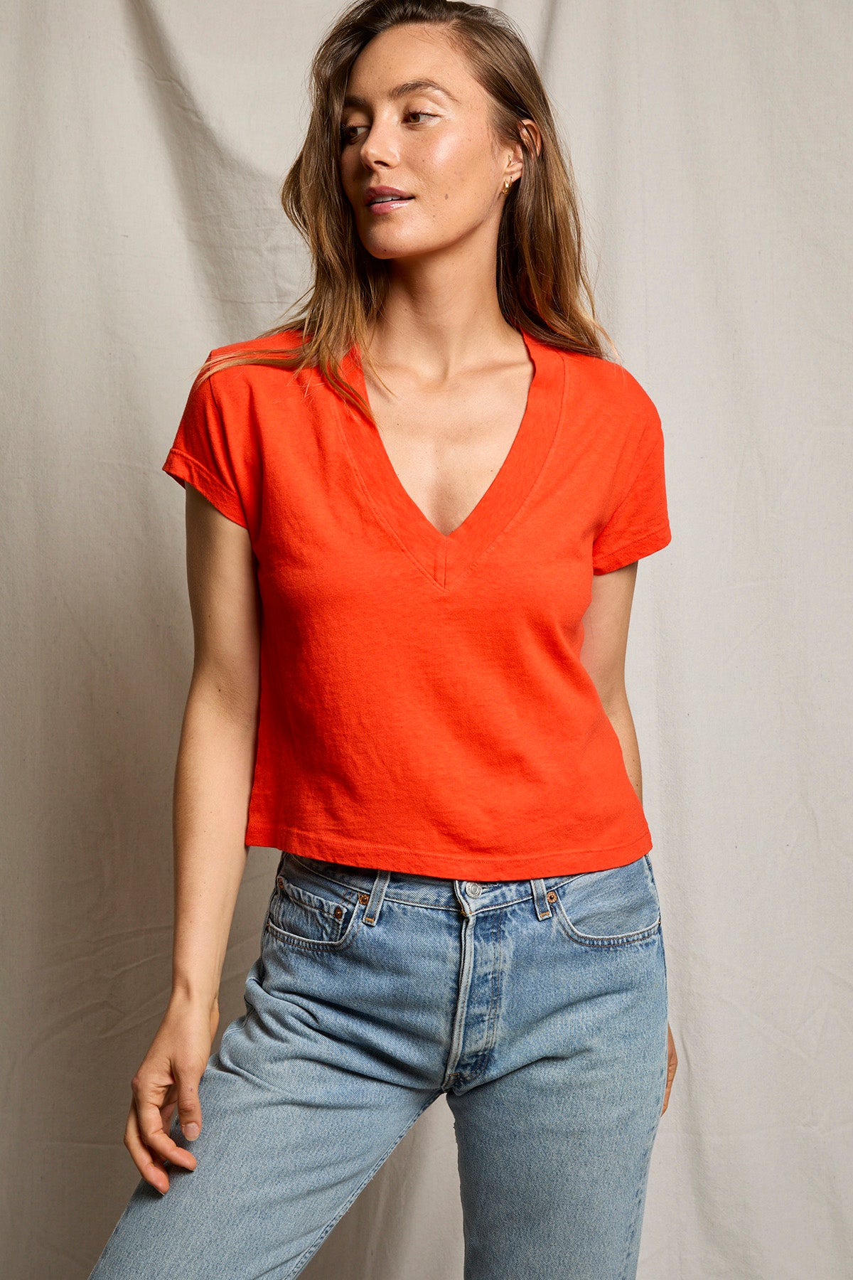 Woman wearing a red shirt and blue jeans against a neutral background