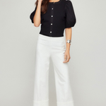 Woman wearing a black top and white pants on a plain background