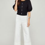 Woman wearing a black top and white pants on a plain background