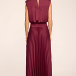 A woman shown from the back wearing a sleeveless pleated maxi dress in a deep burgundy or wine color, paired with beige high-heeled sandals, against a plain light beige studio background.