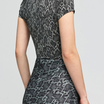 A woman wearing a short-sleeve fit-and-flare dress with a gray and black snakeskin pattern, shown from a rear three-quarter angle against a light gray studio background.