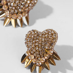 Heart-shaped earrings with gold spikes and crystal embellishments on a light gray background