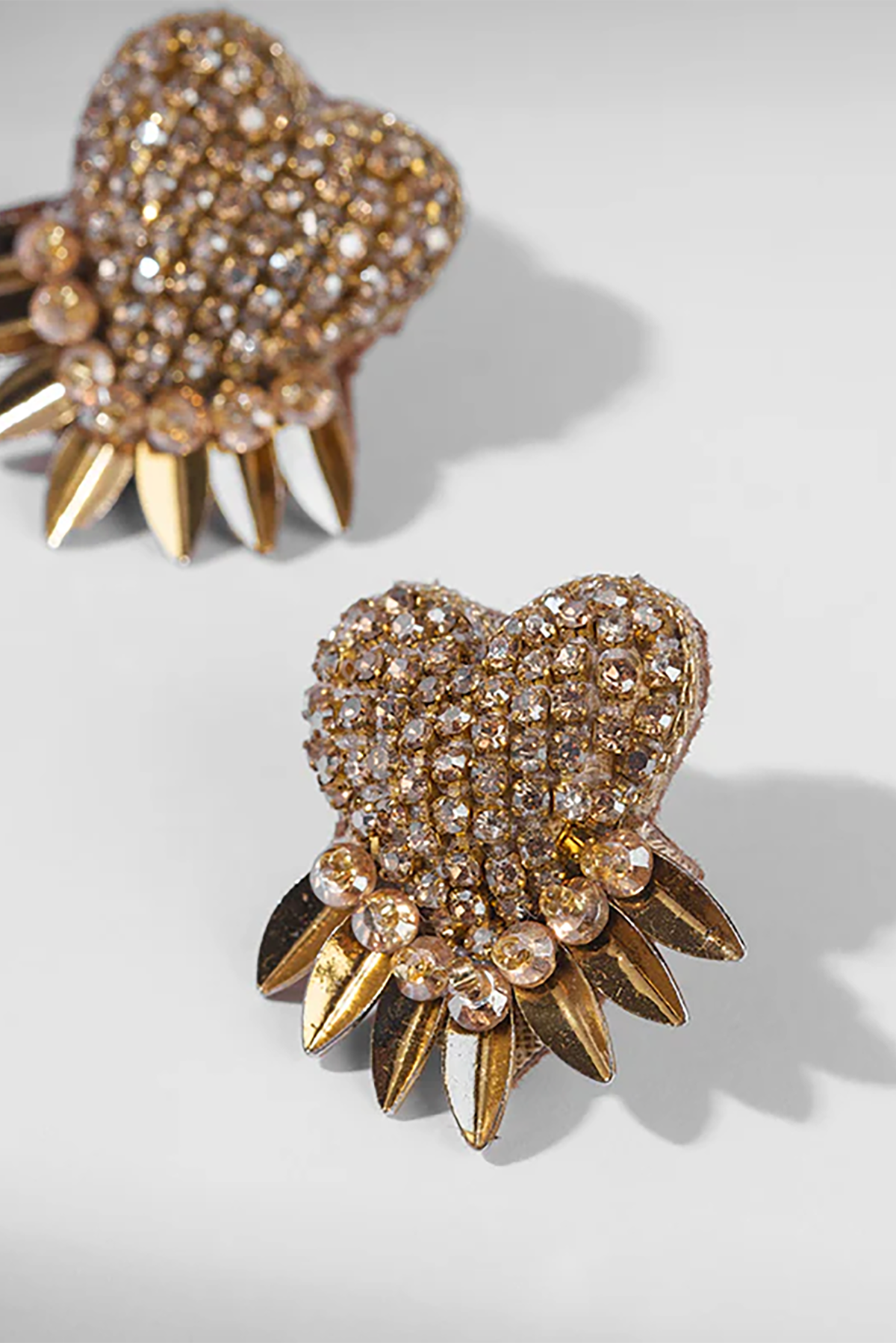 Heart-shaped earrings with gold spikes and crystal embellishments on a light gray background