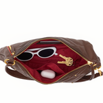 A brown leather shoulder bag shown open against a white background, revealing a red interior lining with white sunglasses, keys, and a small white case inside.