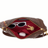 A brown leather shoulder bag shown open against a white background, revealing a red interior lining with white sunglasses, keys, and a small white case inside.