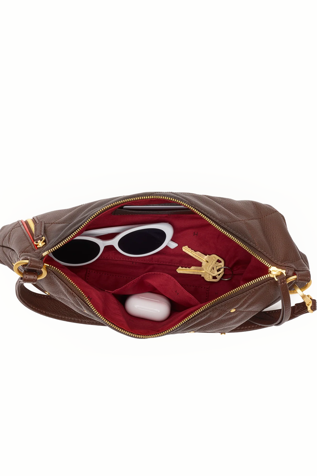 A brown leather shoulder bag shown open against a white background, revealing a red interior lining with white sunglasses, keys, and a small white case inside.