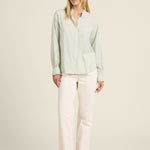 Woman wearing a light green blouse and white pants on a beige background