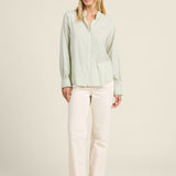 Woman wearing a light green blouse and white pants on a beige background