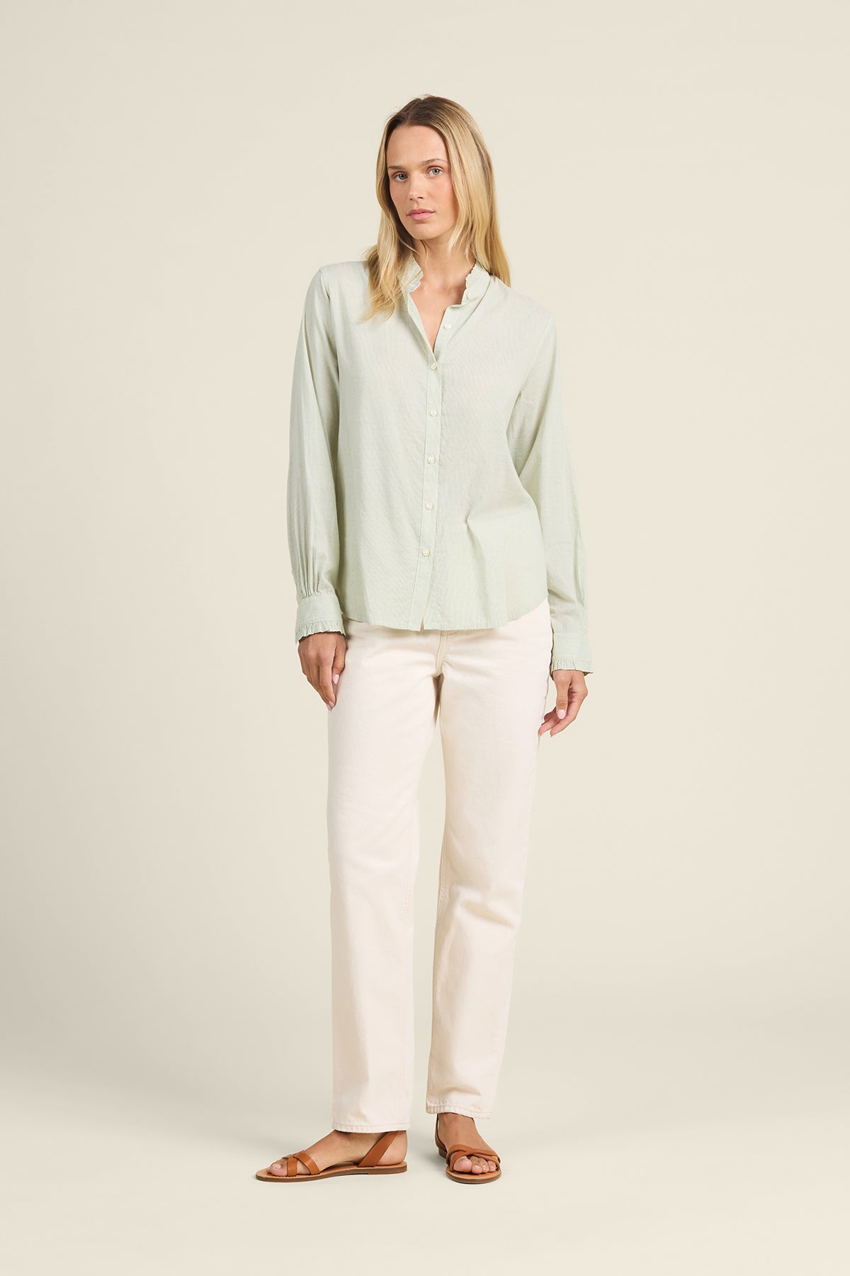 Woman wearing a light green blouse and white pants on a beige background