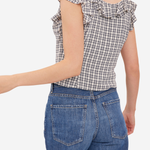 A woman shown from the back wearing a beige and navy gingham check top with ruffled cap sleeves, paired with blue jeans, against a plain white background.