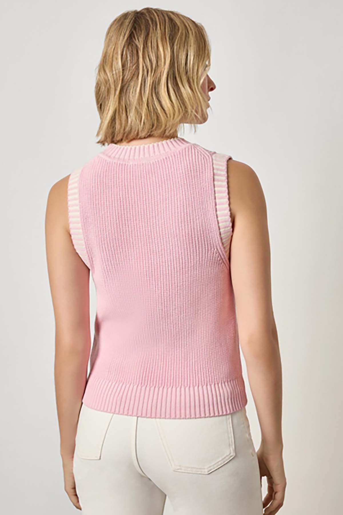 Woman wearing a pink sleeveless sweater against a plain background